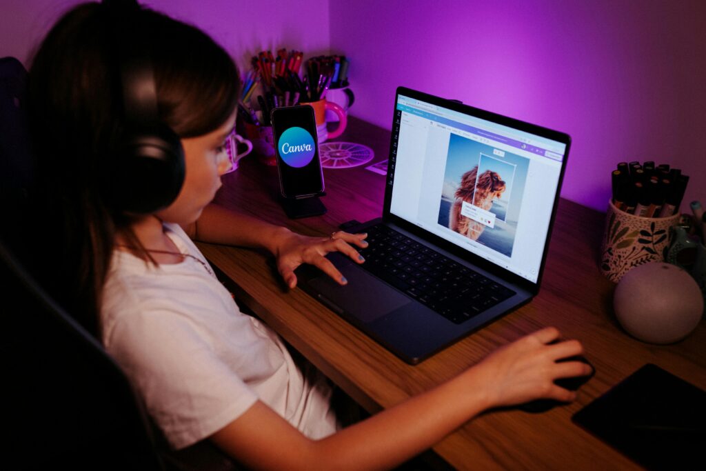 Young girl using a laptop with headphones under purple lighting, focused on photo editing.